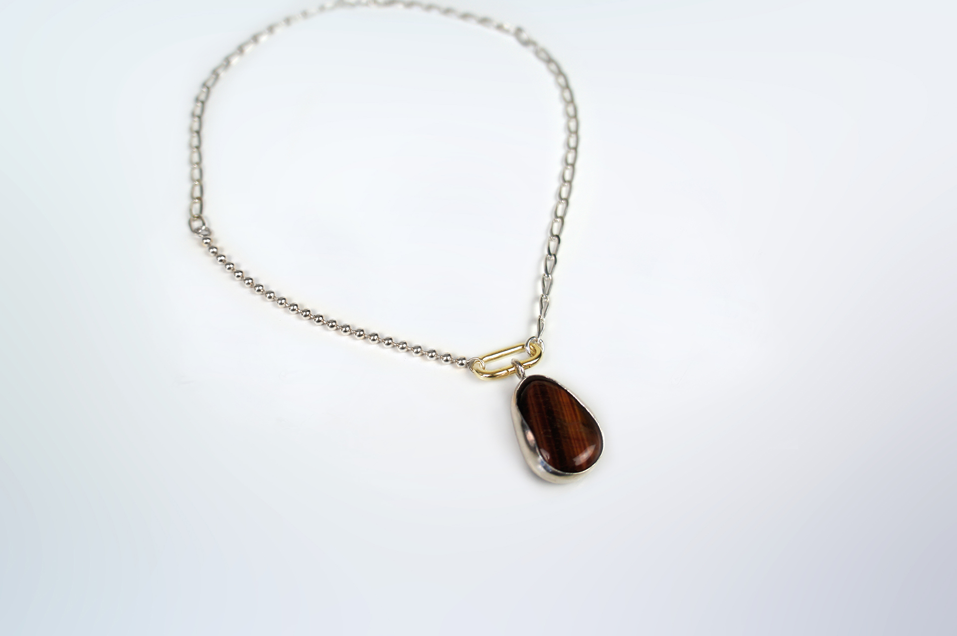 Rokku statement necklace in silver with tiger's eye stone pendant and gold plated clasp.